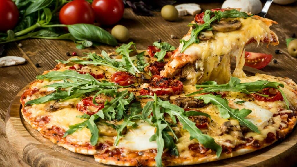 Gourmet pizza with rocket and tomatoes on wooden board.
