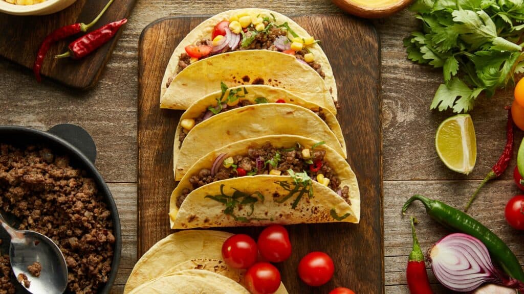 Fresh beef tacos with vegetables on wooden table.